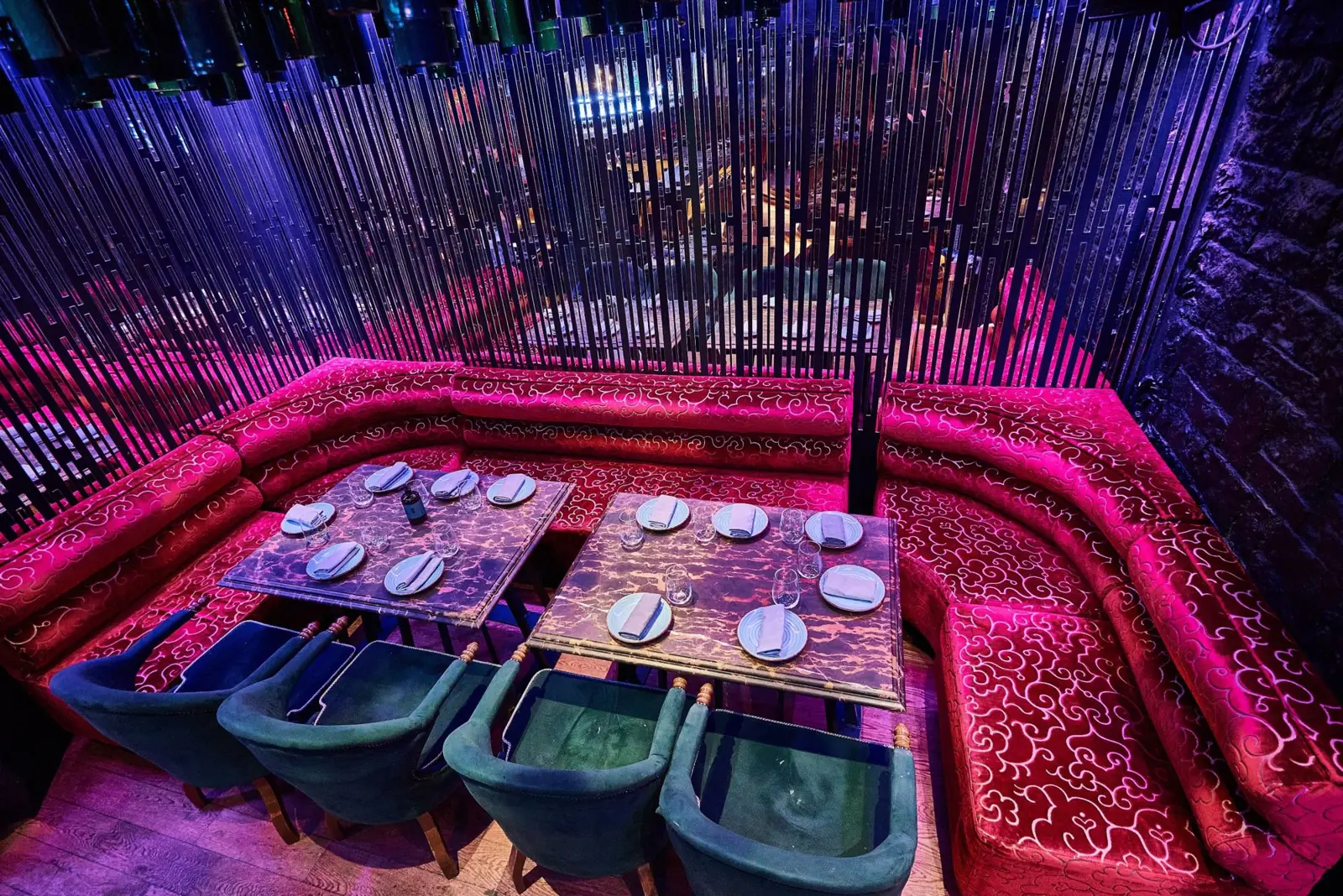Magenta velvet banquettes behind a curtain of mirrored slats